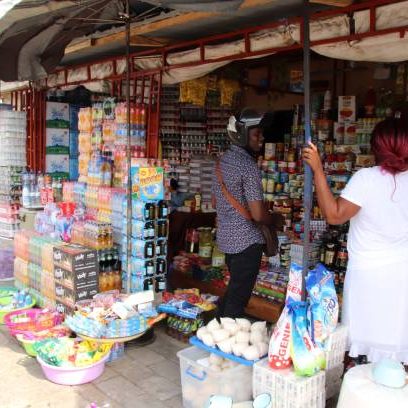 Avepozo, Togo - February 26, 2019: Kiosk sells food and drinks in the rural area of the village Avepozo, Togo, West Africa. A customer with a crash helmet buys from a female vendor.